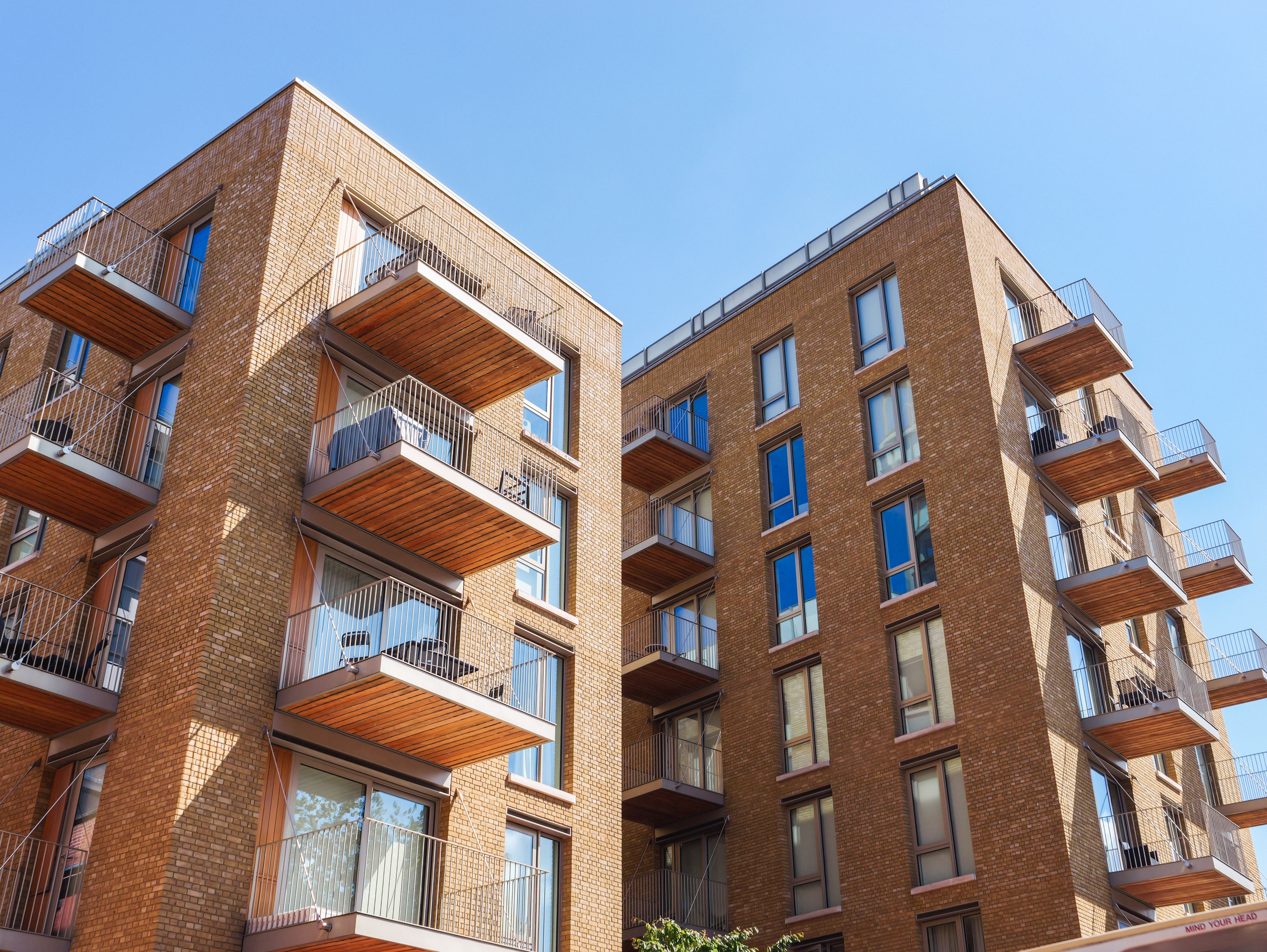 Modern apartment building with brick exterior, large windows, and wooden balconies under a clear blue sky.