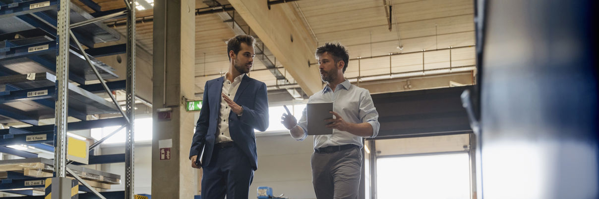 Businessman And Colleague With Digital Tablet Talking While Walking At Factory
