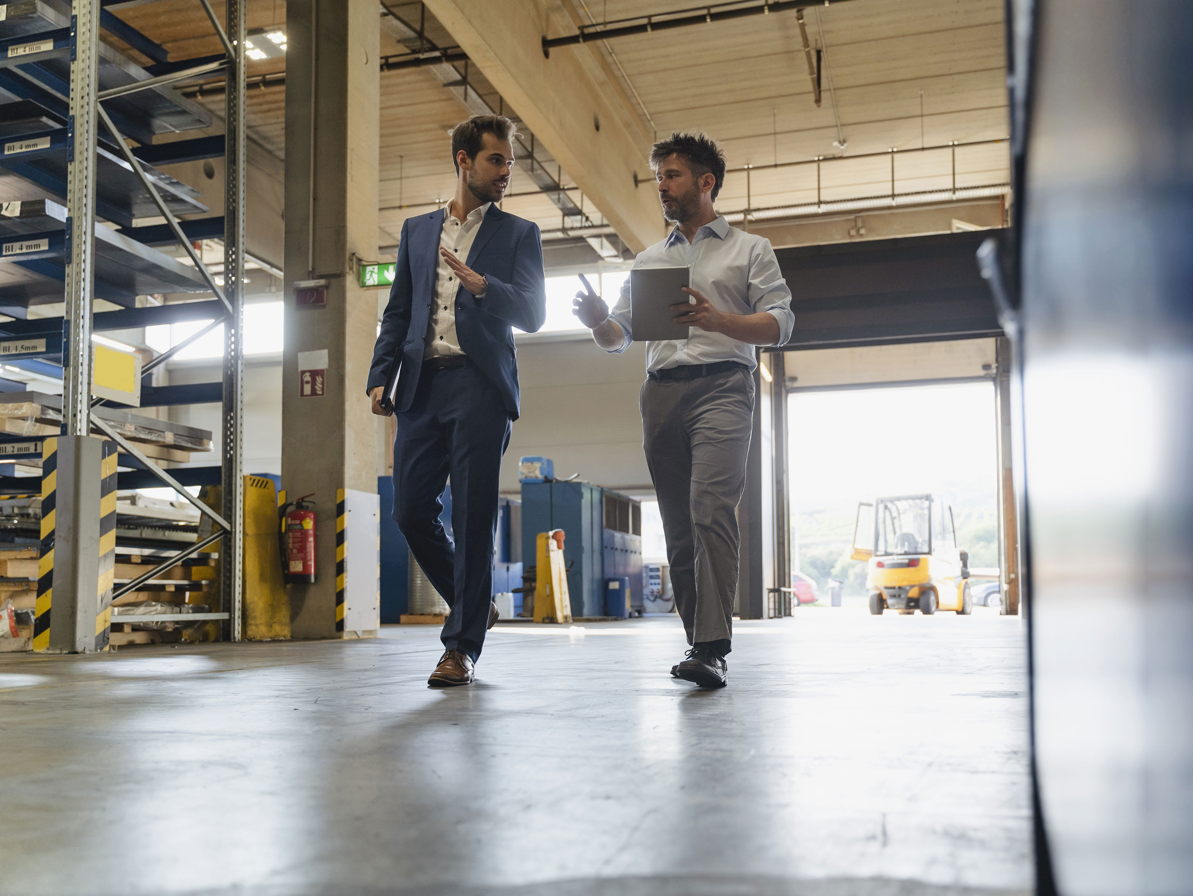 Businessman And Colleague With Digital Tablet Talking While Walking At Factory