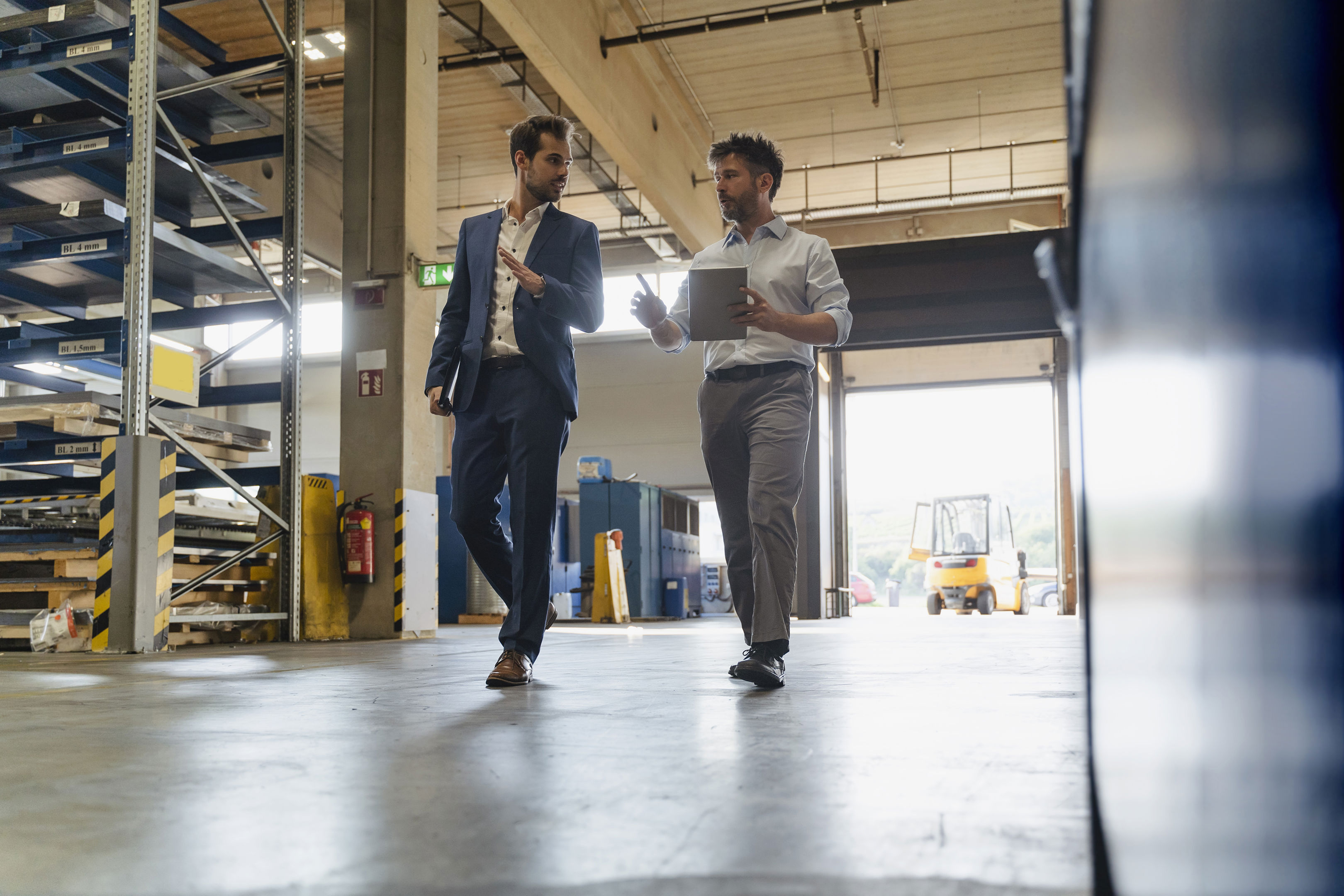 Businessman And Colleague With Digital Tablet Talking While Walking At Factory
