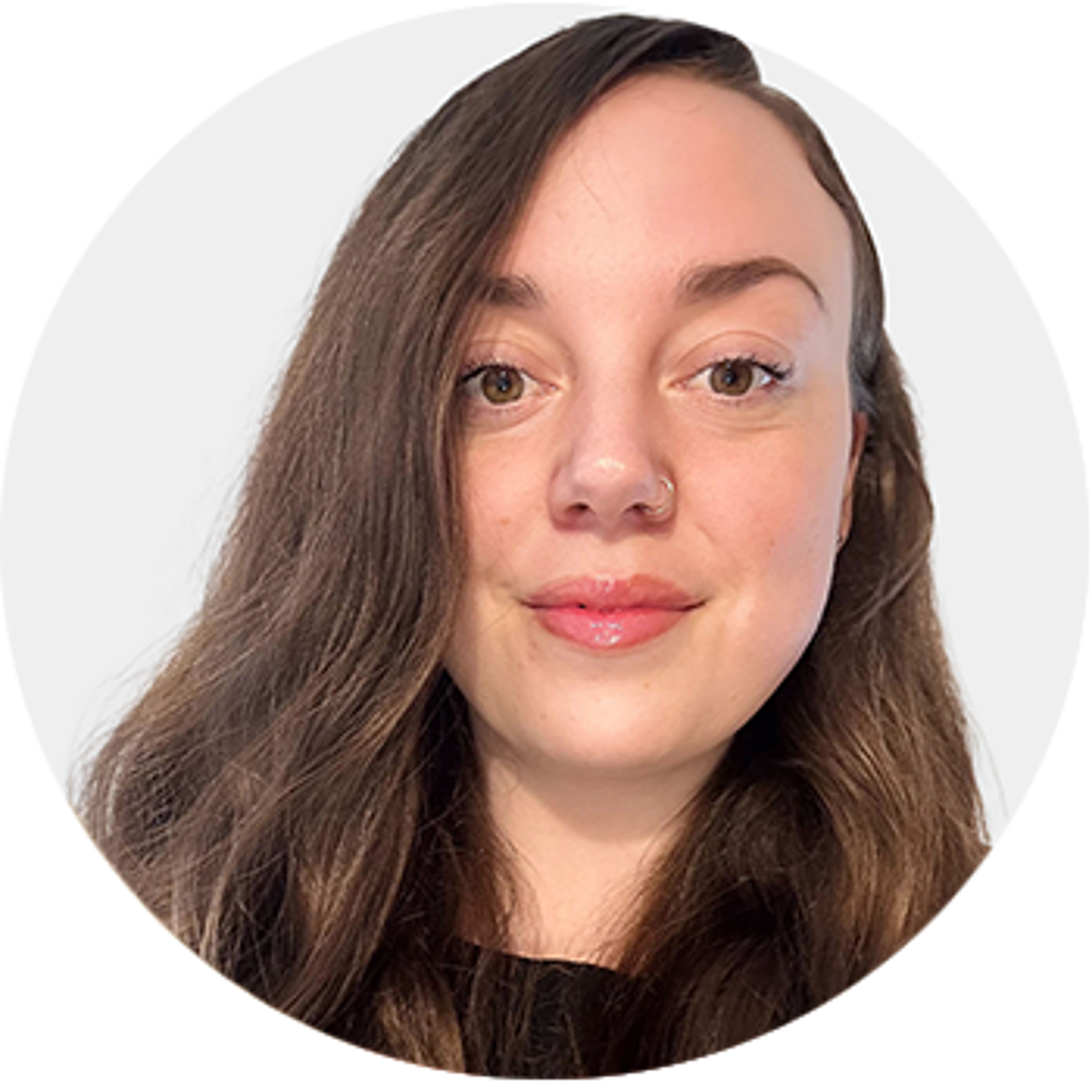 A woman with long brown hair, fair skin, and a nose ring smiles softly at the camera. She is wearing a black top, and the background is a plain light grey.