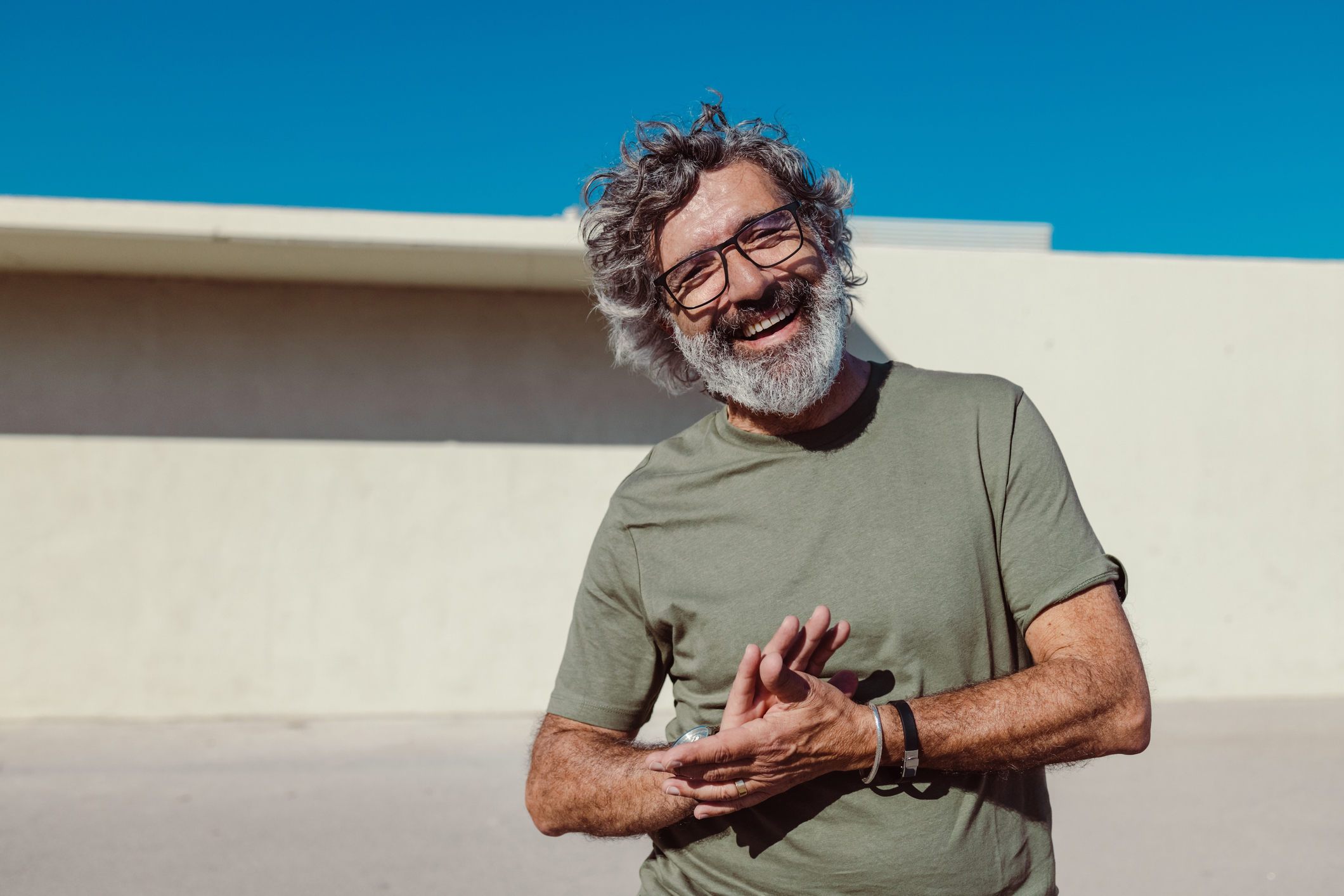 Man with glasses and beard standing in sun smiling clapping hands
