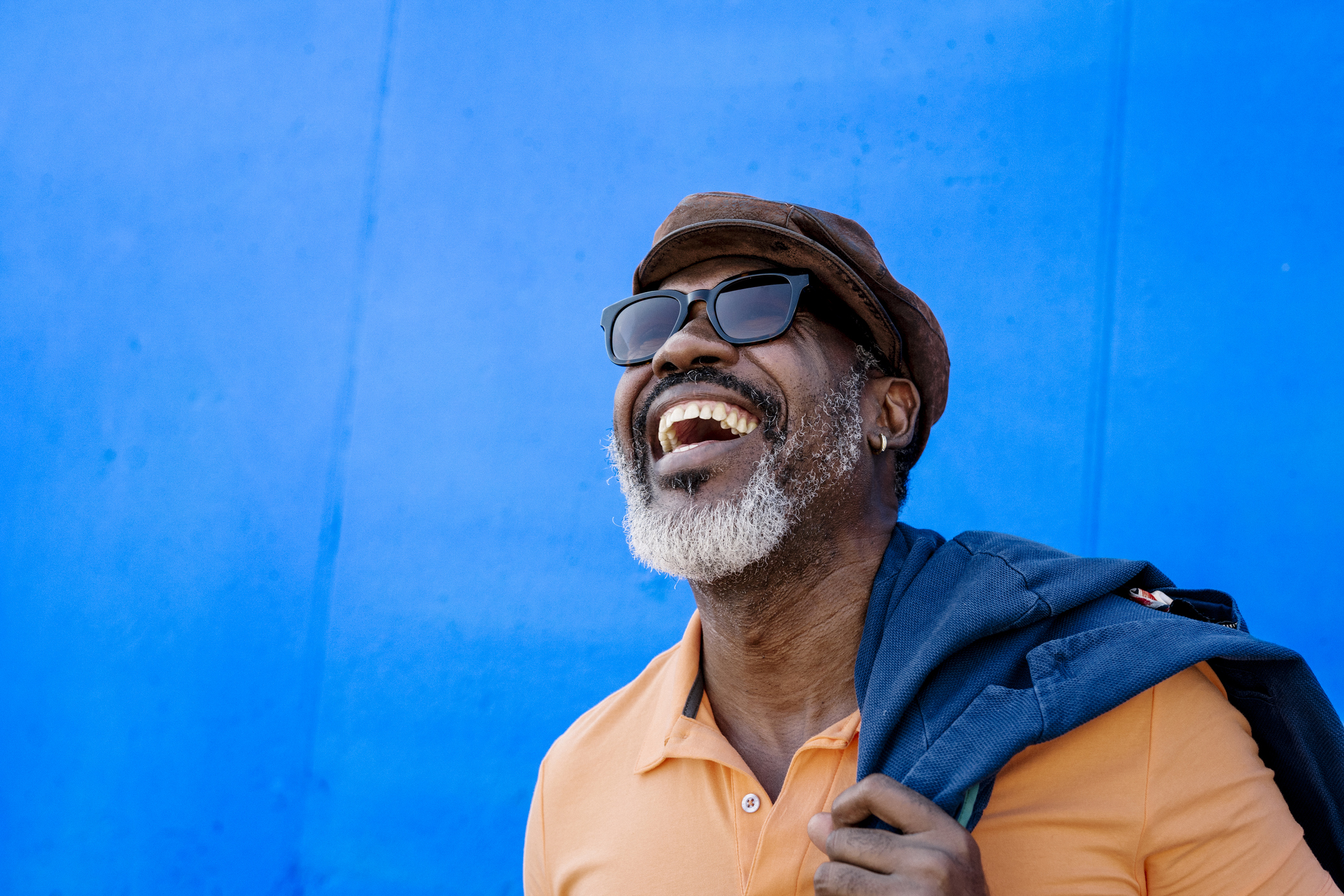 Middle-aged man with hat and sunglasses on standing in front of electric blue wall