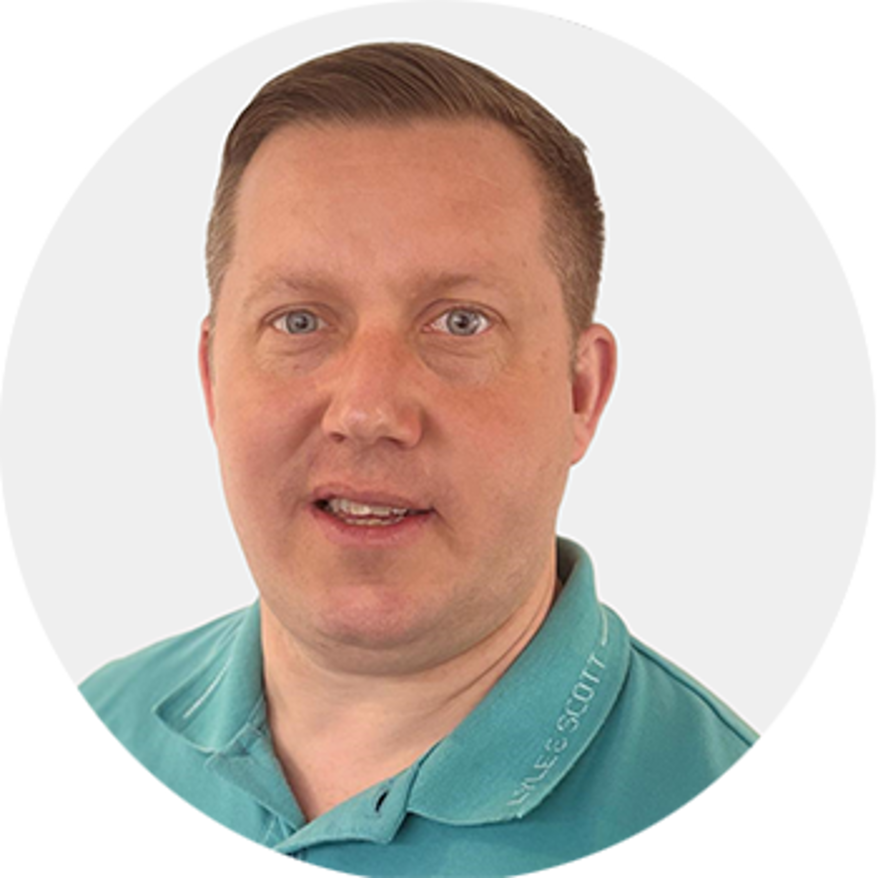 A man with short light brown hair wearing a teal collared shirt looks at the camera with a neutral expression. The background is plain white.