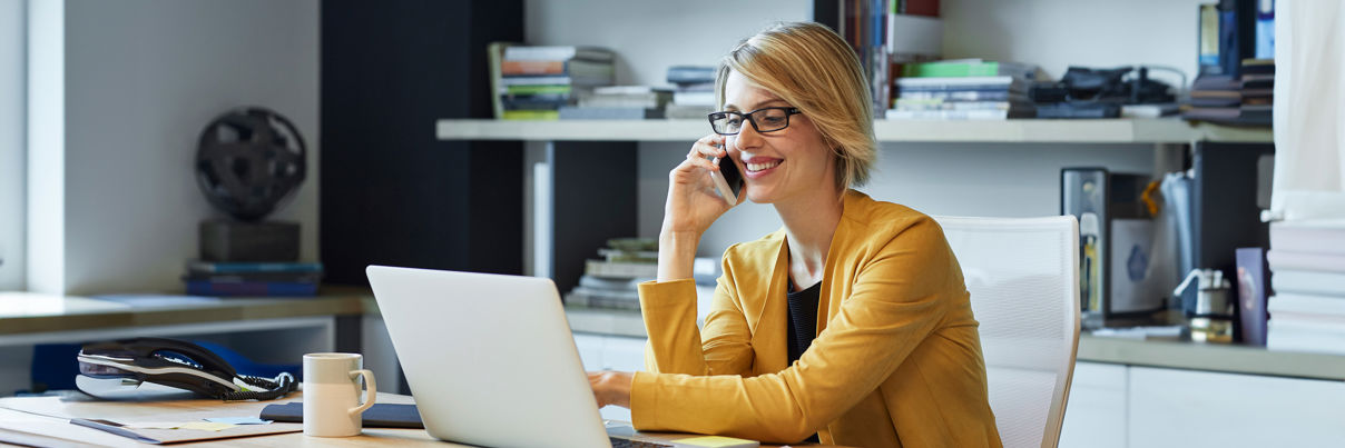 Businesswoman Using Laptop And Smart Phone At Desk
