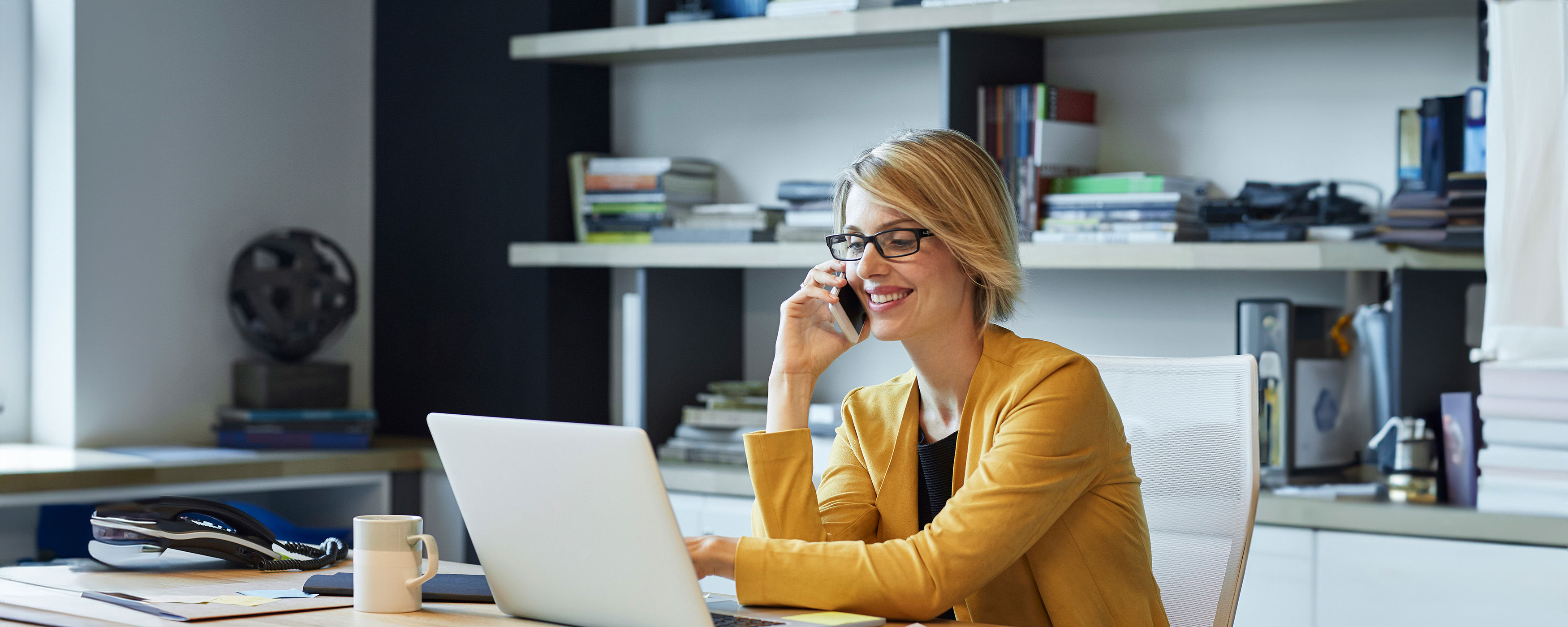 Businesswoman Using Laptop And Smart Phone At Desk