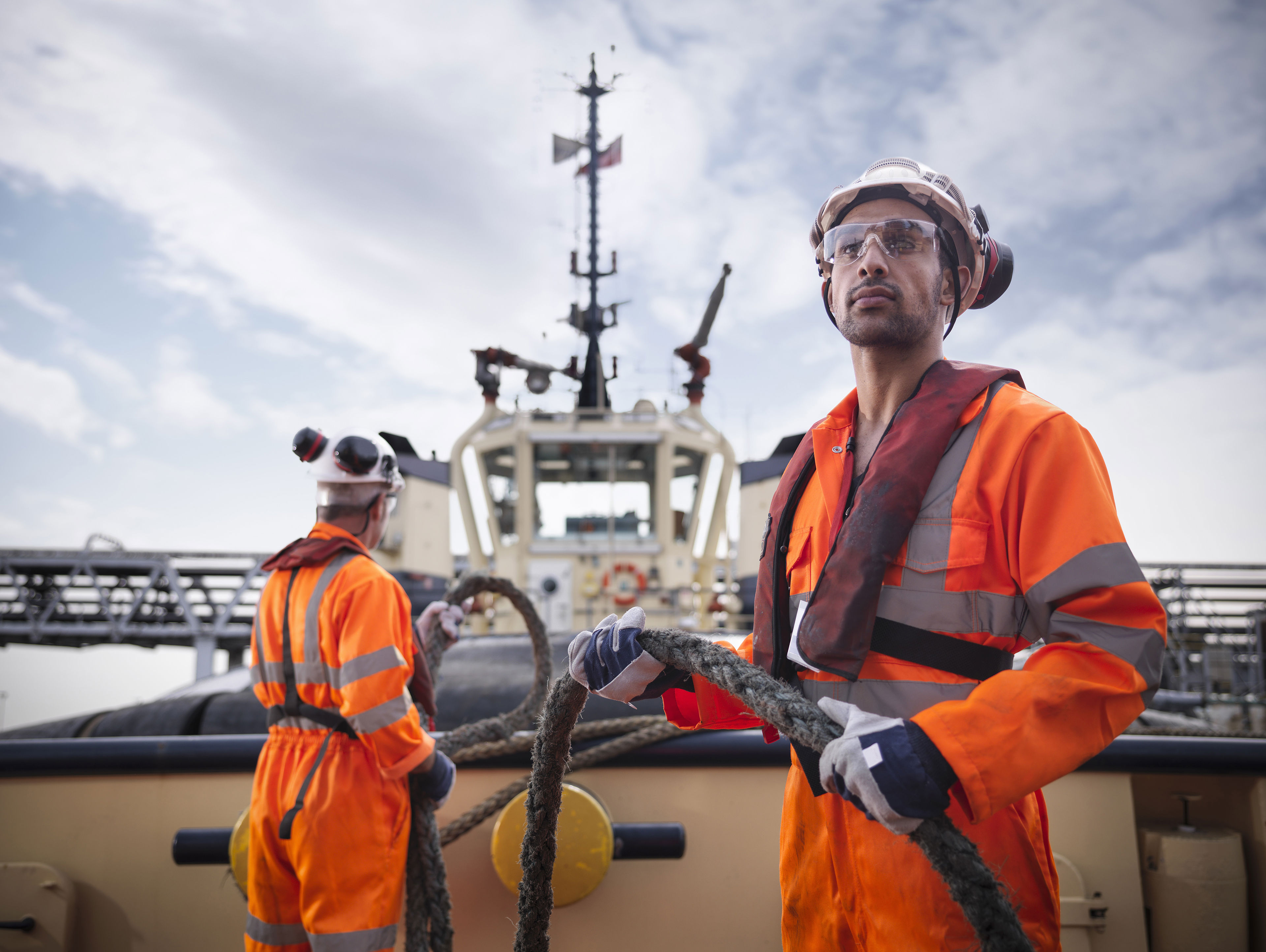 Tug Workers Wearing Protective Clothing Holding Rope On Tug