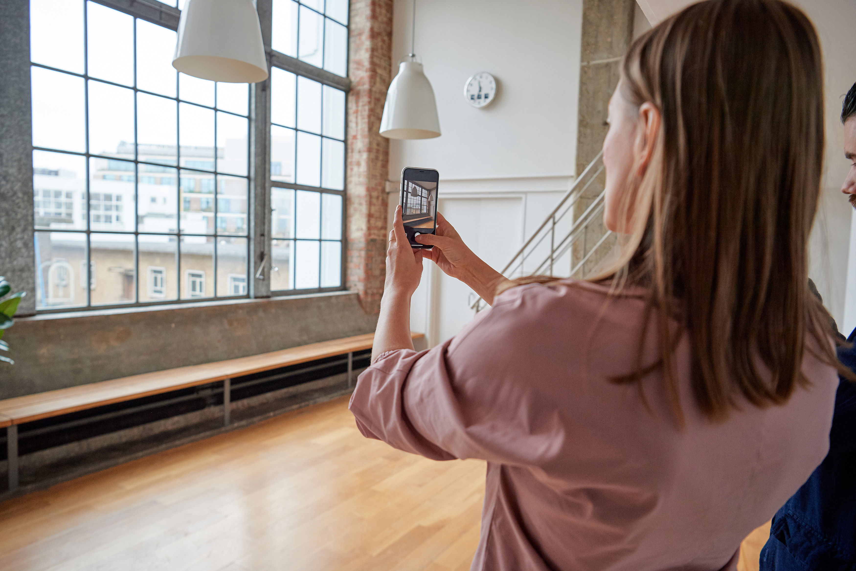 A woman holding up a smart phone and taking a photo of a window from within an empty apartments.