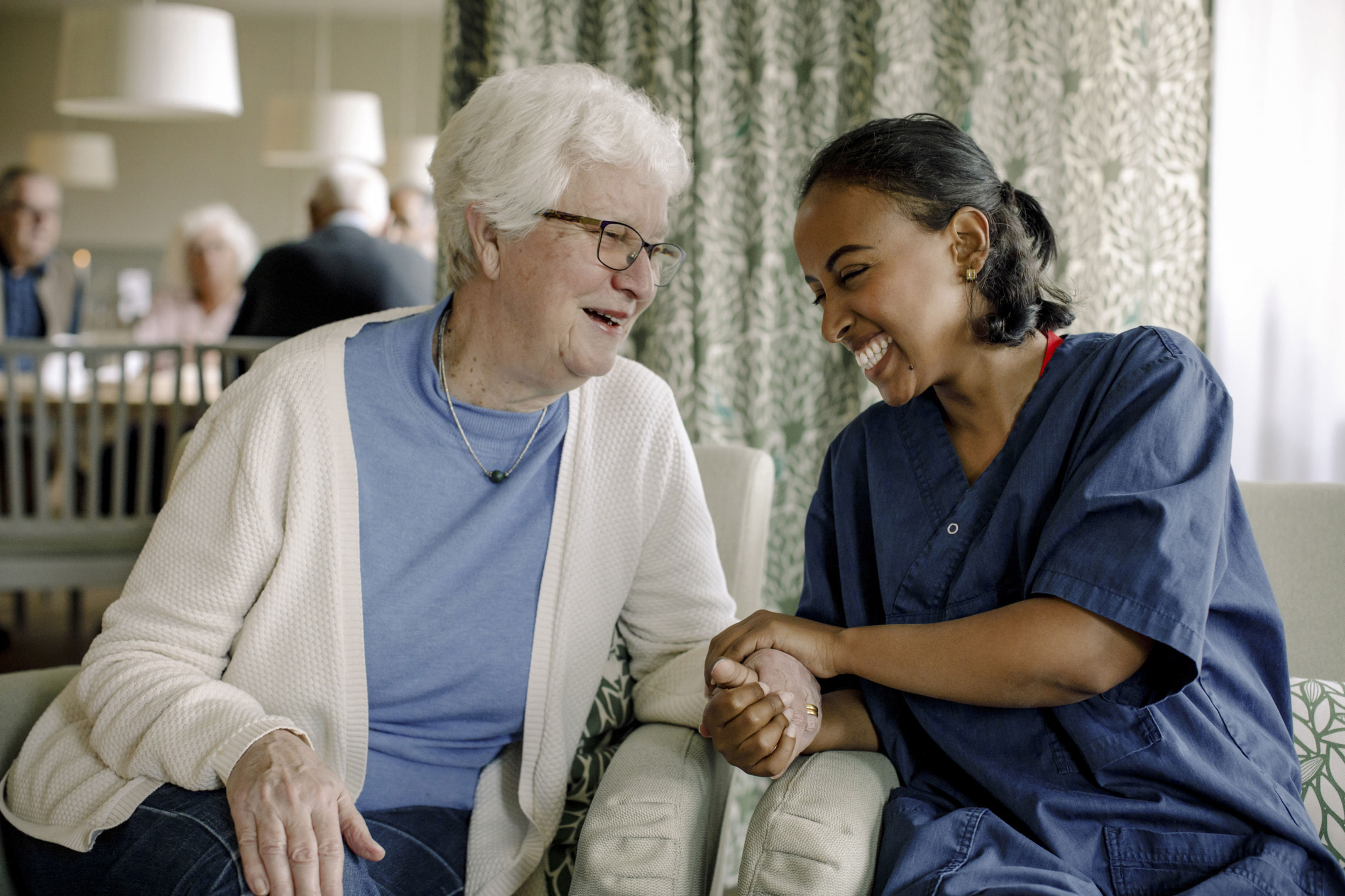 Cheerful female nurse holding hand of senior woman sitting at retirement home