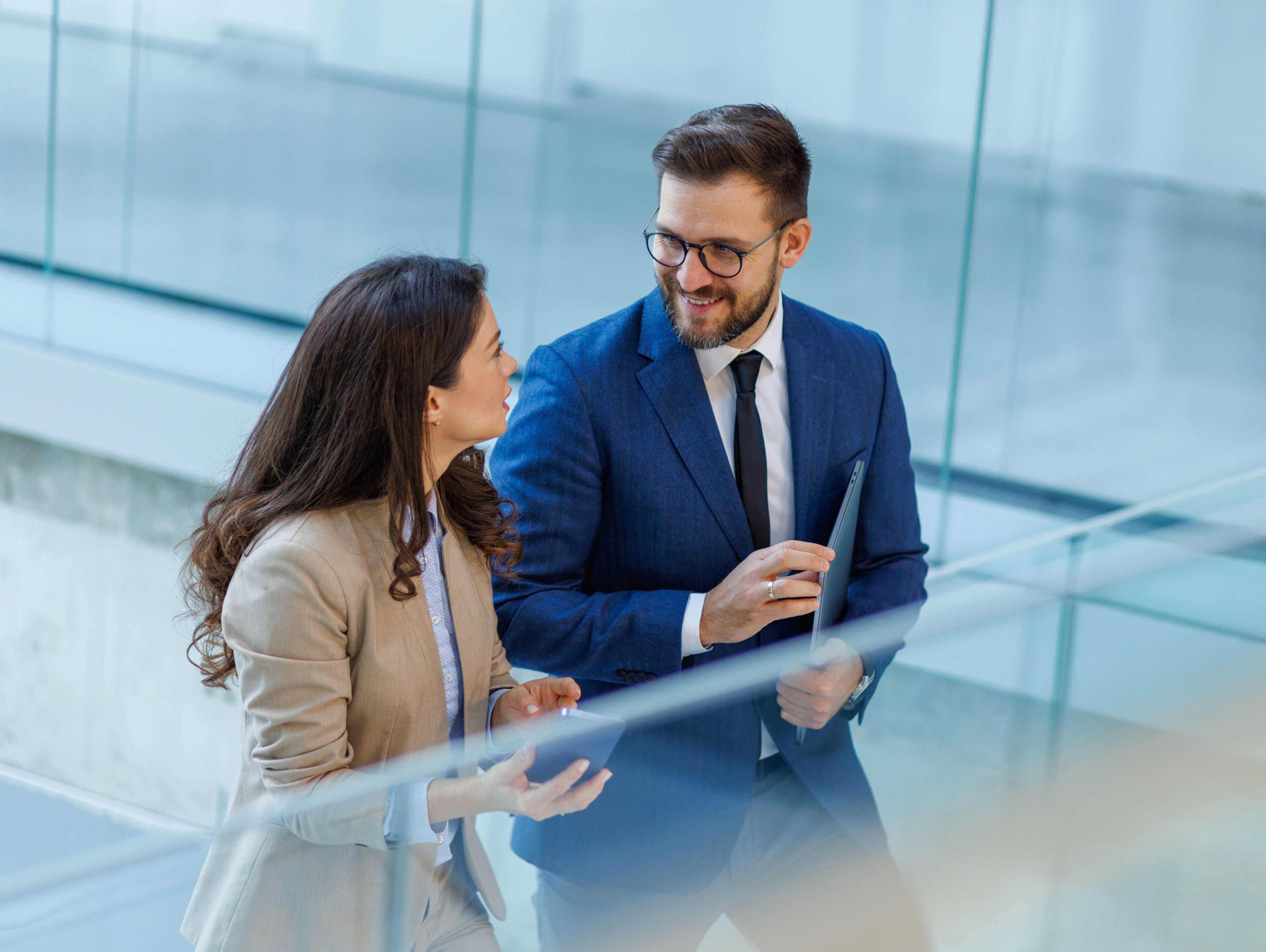 A man and woman in business attire walking and talking in an office building.