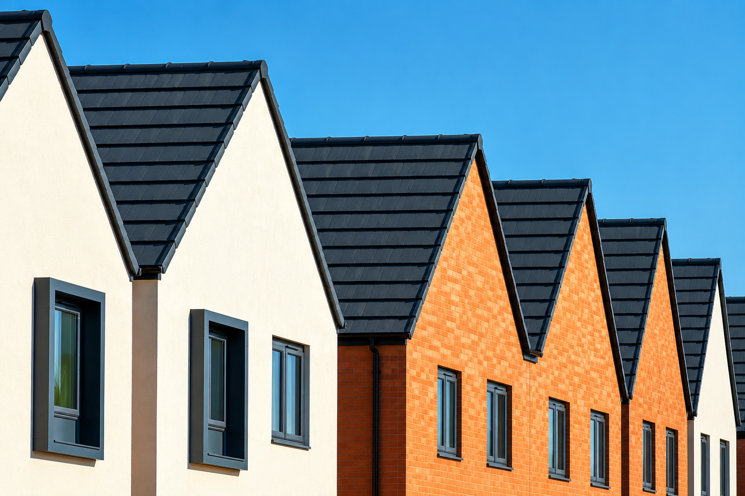 Row of modern houses with pitched roofs, featuring alternating white and orange brick exteriors, dark-framed windows, and a clear blue sky in the background.