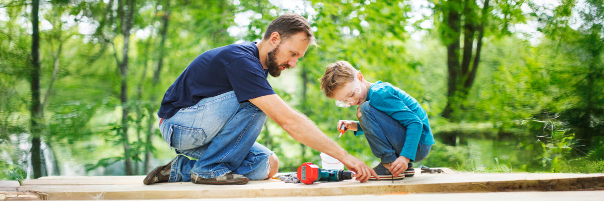 A person in a yellow raincoat stands on a rocky, misty shore looking out at the ocean, with grey clouds above and waves crashing against the rocks.