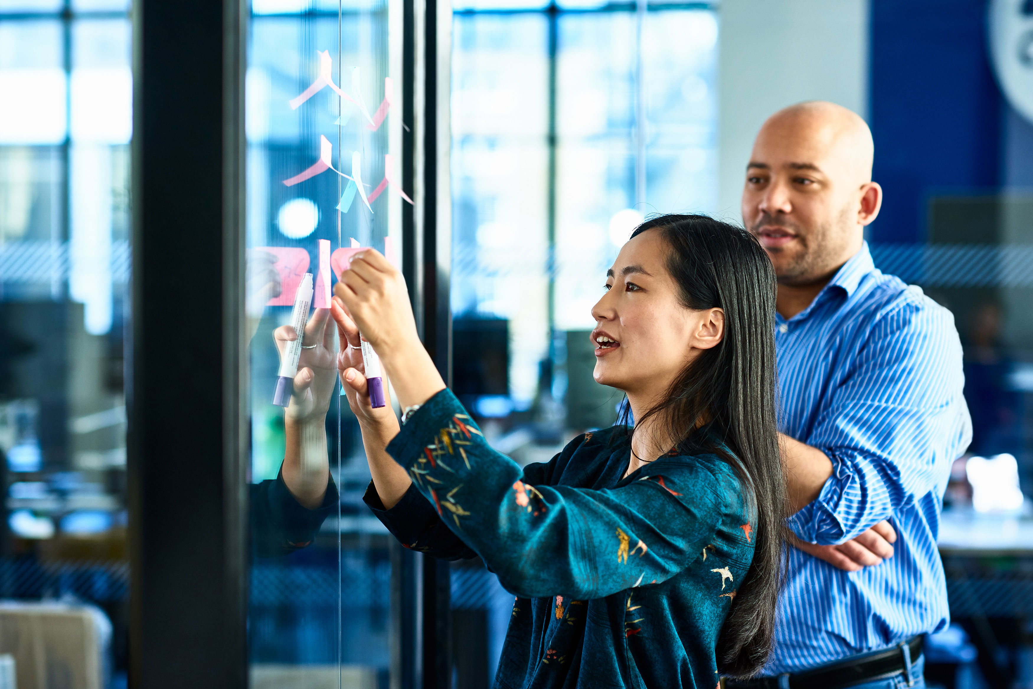 Businesswoman Sticking Notes On Glass With Colleague
