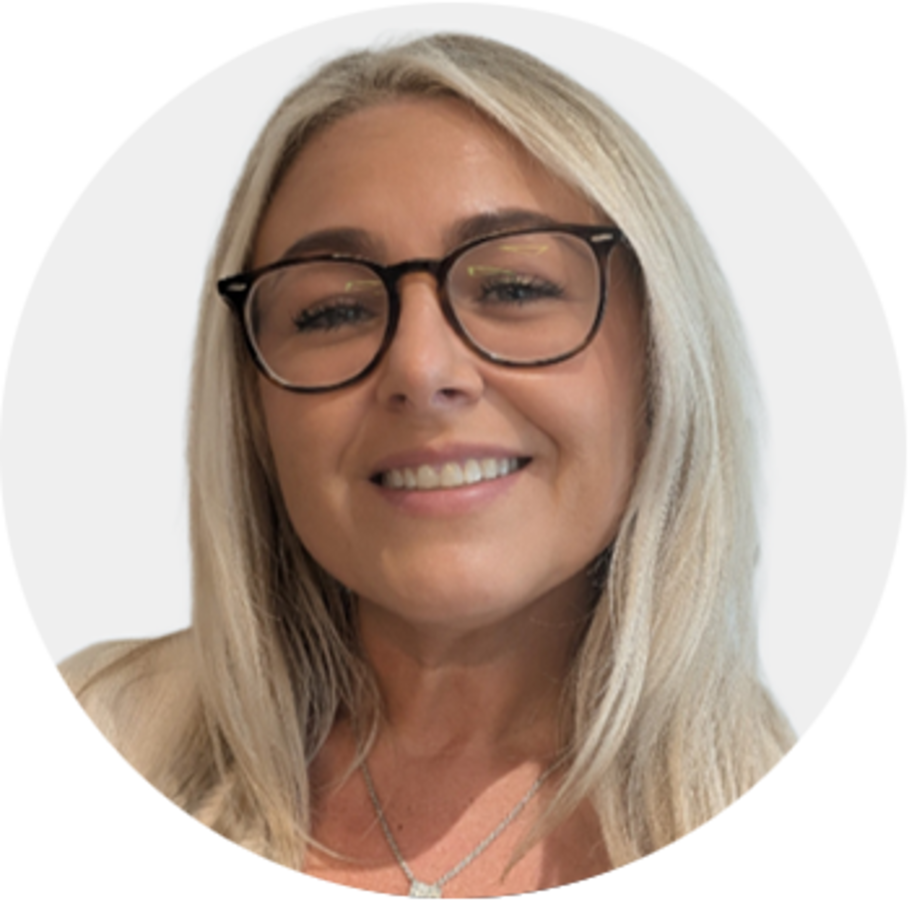 Smiling woman with long blonde hair and black-rimmed glasses, wearing a light-colored top and necklace, in front of a plain, light background.
