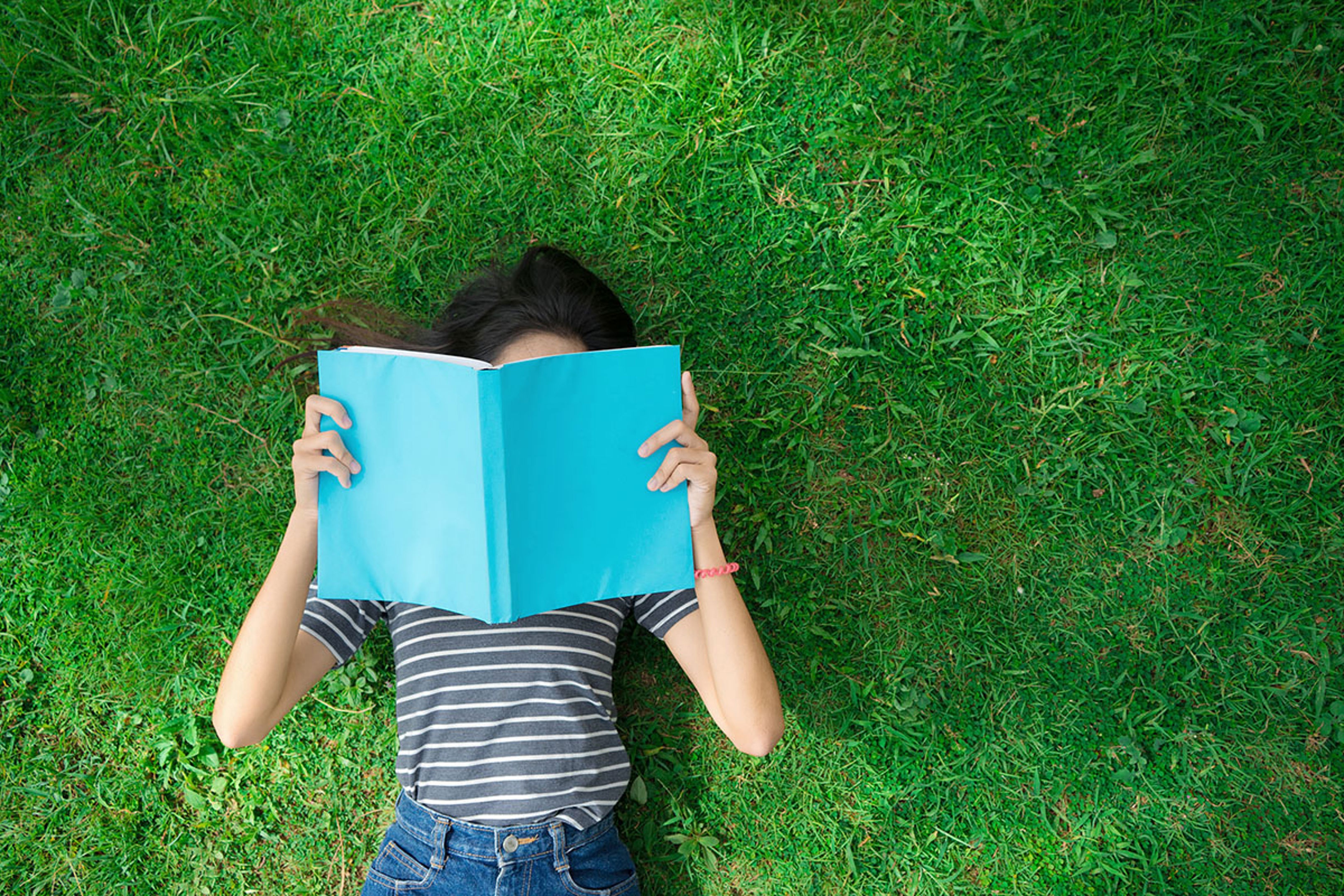 Woman Lying On Grass Reading Blue Book