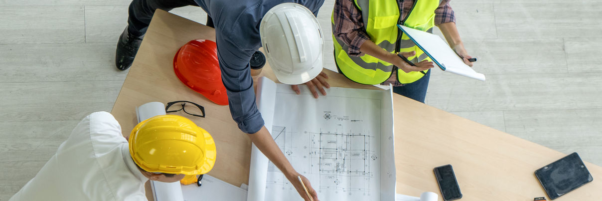 High Angle Photo From Directly Above Of An Architect, A Businessman, And A Construction Worker Examining A Blueprint On A Construction Site.