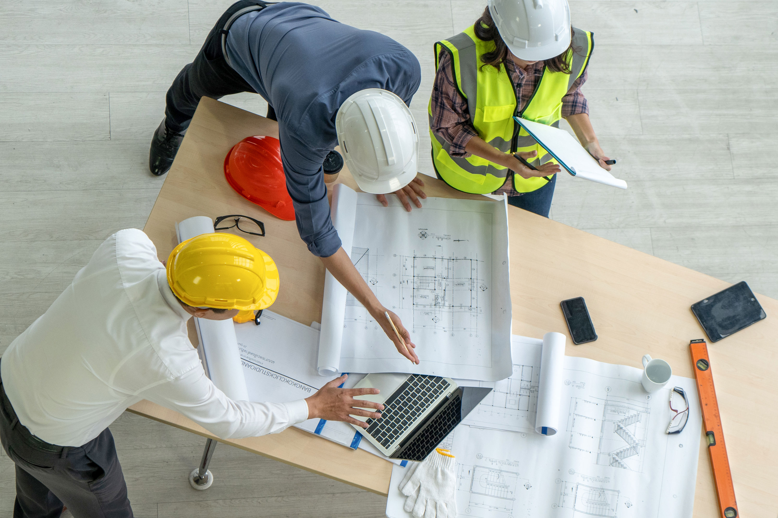 High Angle Photo From Directly Above Of An Architect, A Businessman, And A Construction Worker Examining A Blueprint On A Construction Site.