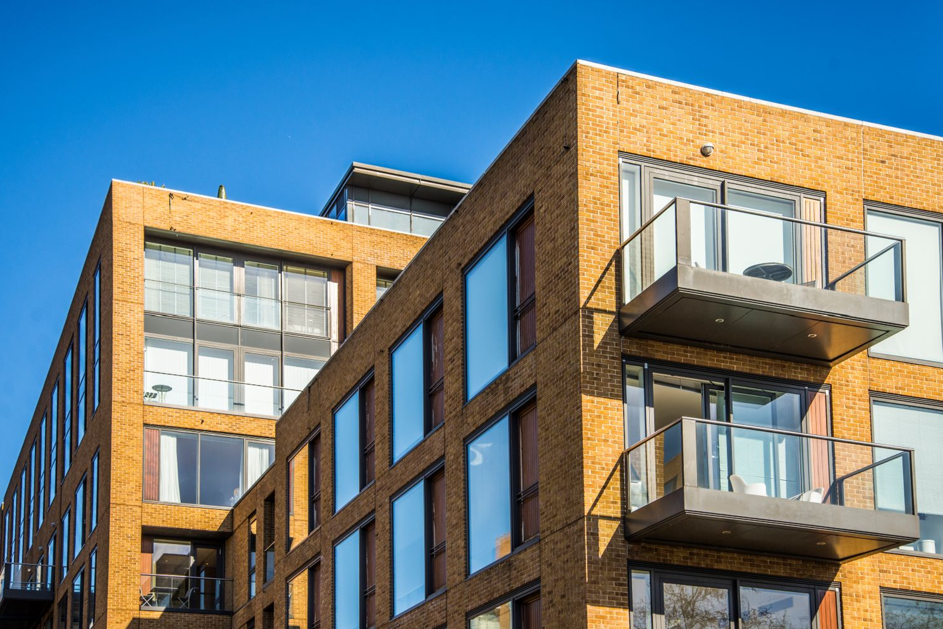 Modern apartment building with large windows and glass balconies, featuring a yellow-brown brick exterior under a clear blue sky.