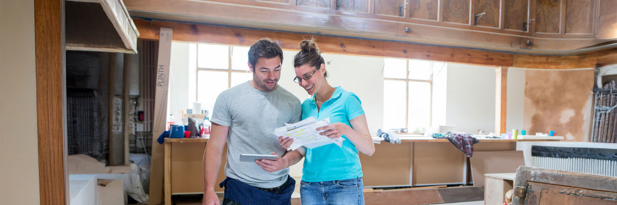 A man and woman looking at property plans on paper and smiling.