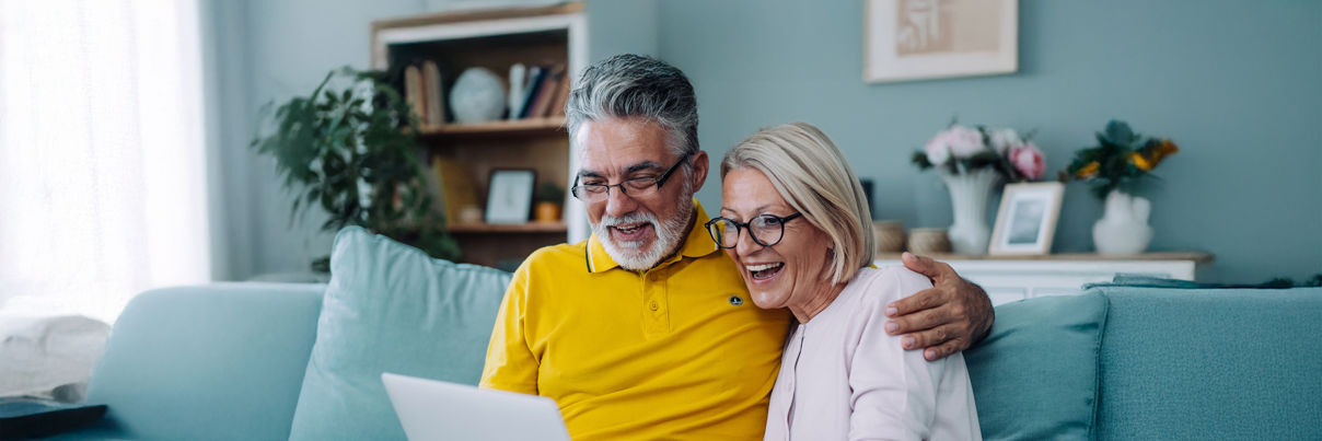 A man and woman sitting on a couch looking at a laptop.