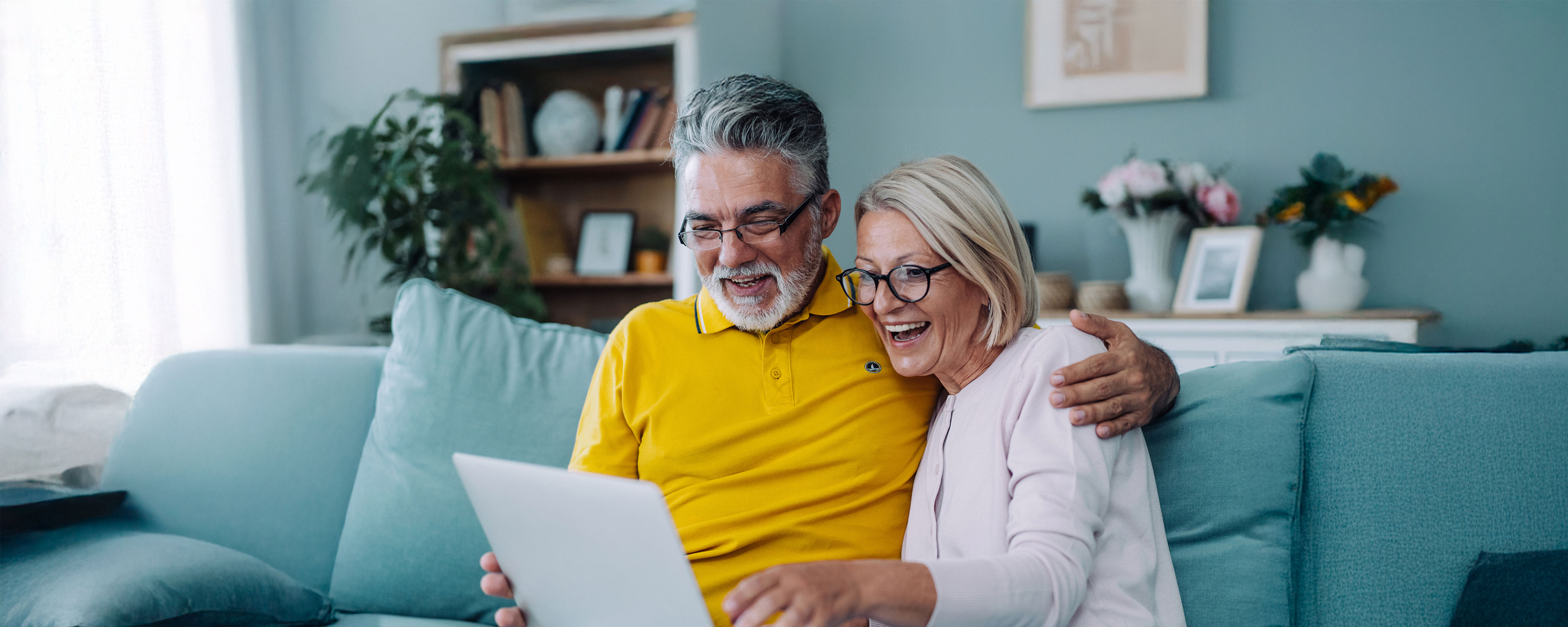 A man and woman sitting on a couch looking at a laptop.