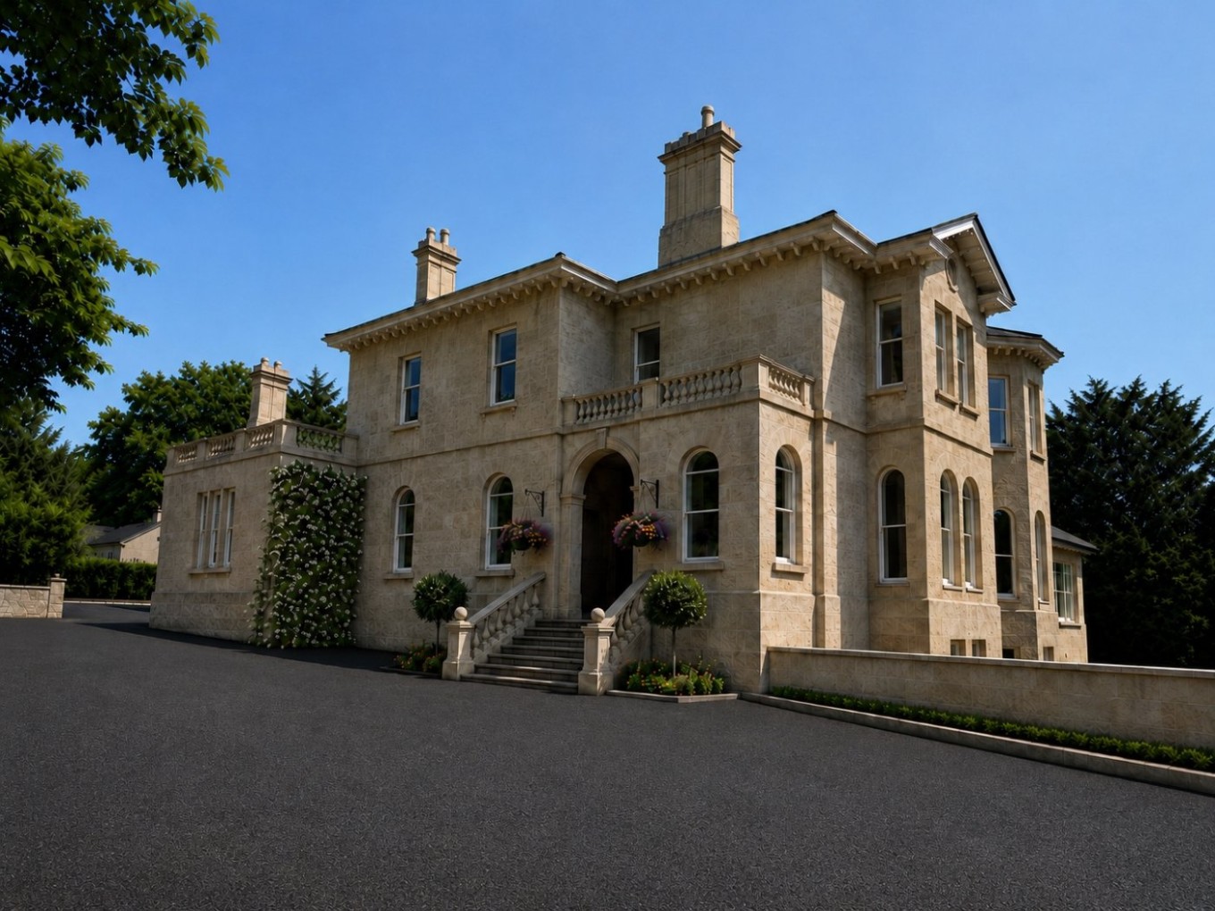 Large cream-colored mansion with arched windows, decorative stonework, and a grand stairway entrance. The house is surrounded by greenery and sits under a clear blue sky.