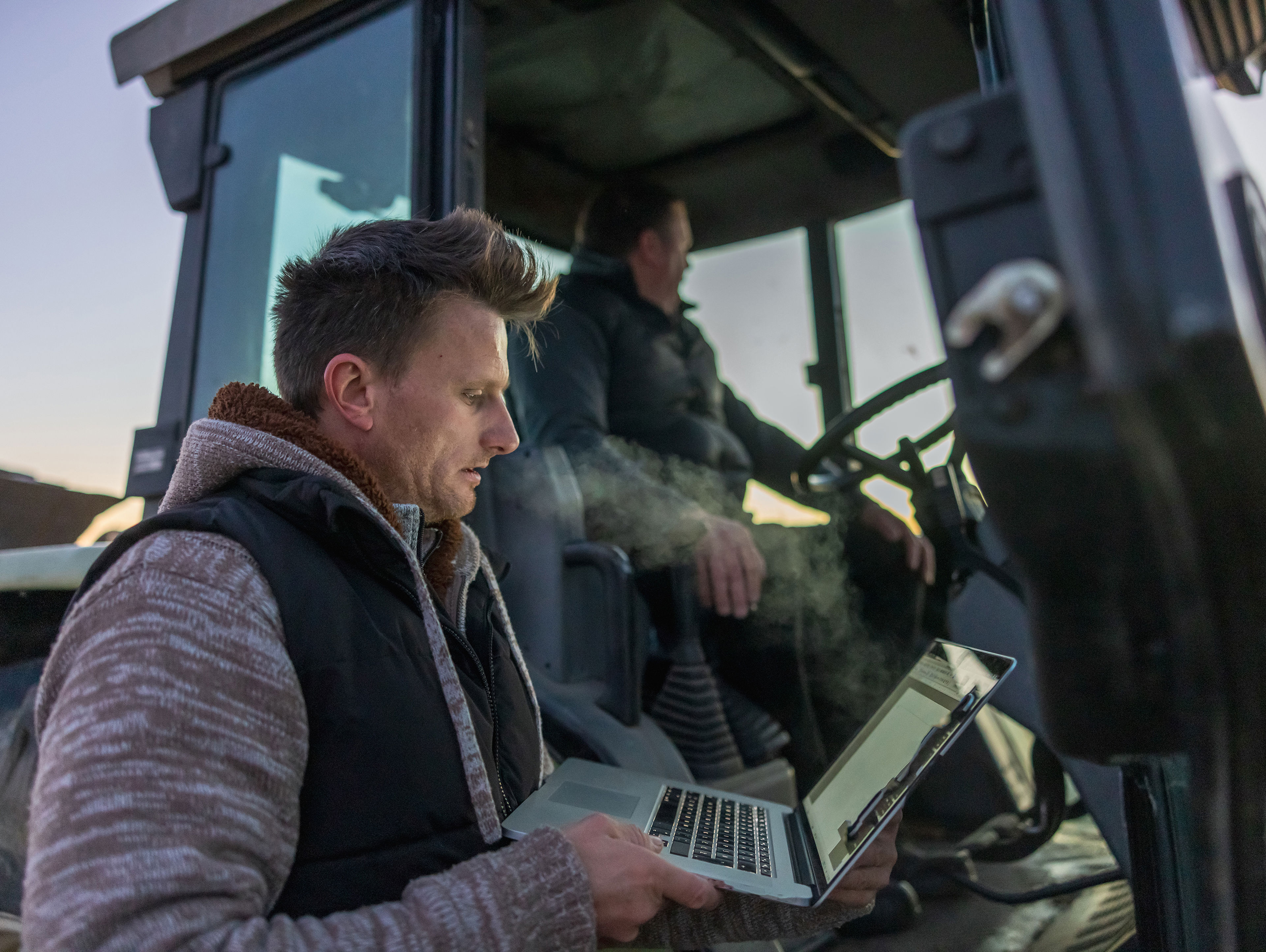 Farmer Using Laptop While Standing Next To A Tractor